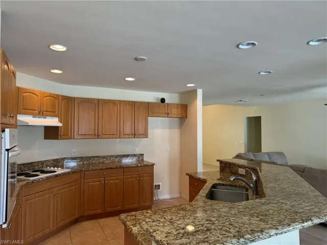 Kitchen featuring sink, dark stone countertops, light tile patterned floors, and white appliances