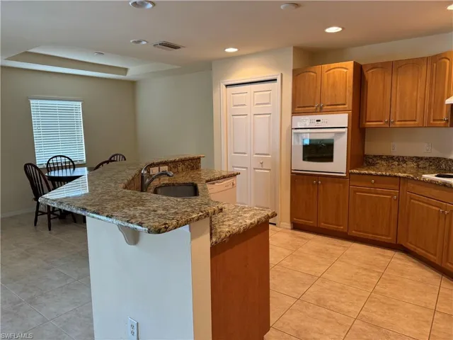 Kitchen featuring dark stone countertops, sink, white appliances, and light tile patterned floors