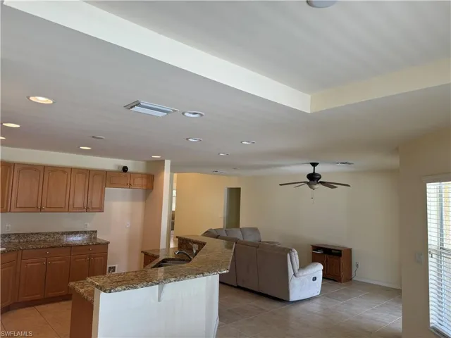 Kitchen featuring light tile patterned flooring, dark stone counters, sink, and ceiling fan
