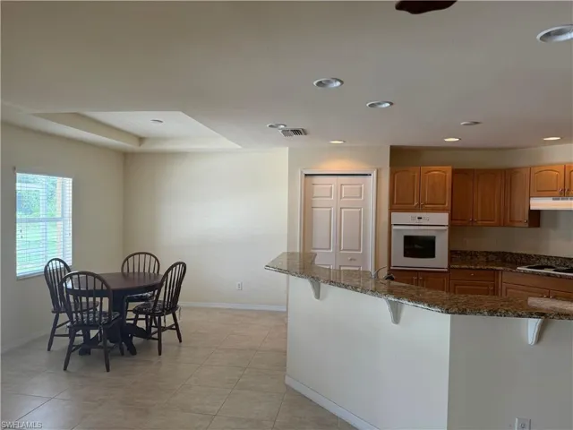 Kitchen with electric stovetop, dark stone countertops, a breakfast bar area, white oven, and light tile patterned floors