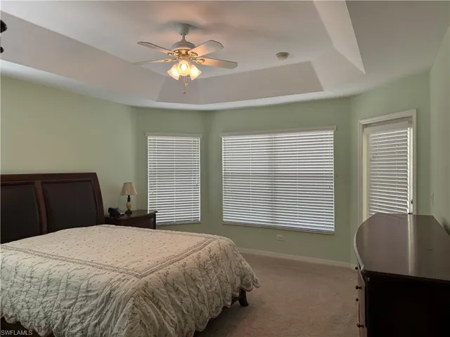 Bedroom with carpet flooring, a raised ceiling, and ceiling fan