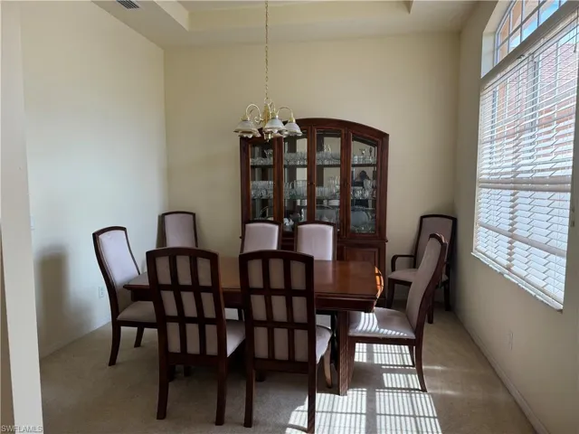 Dining area with carpet flooring, a notable chandelier, and a tray ceiling