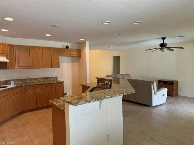 Kitchen with cooktop, ceiling fan, stone counters, sink, and light tile patterned floors