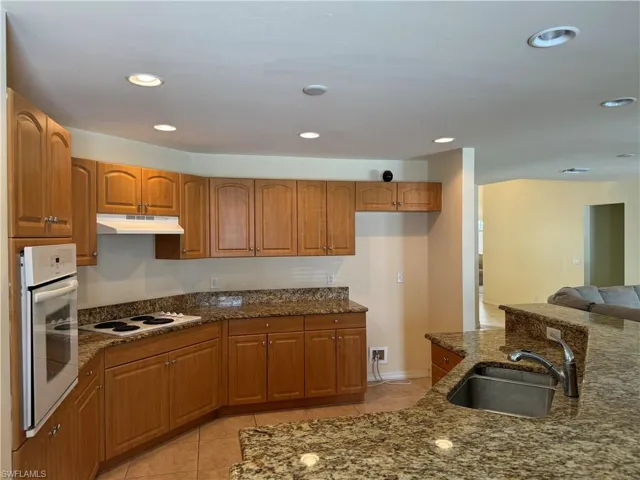 Kitchen with dark stone counters, light tile patterned floors, white appliances, and sink