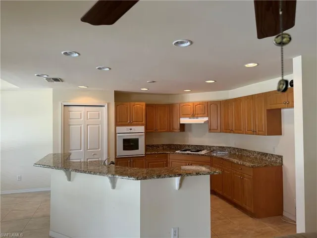 Kitchen featuring white appliances, dark stone countertops, a kitchen island, a breakfast bar, and light tile patterned floors