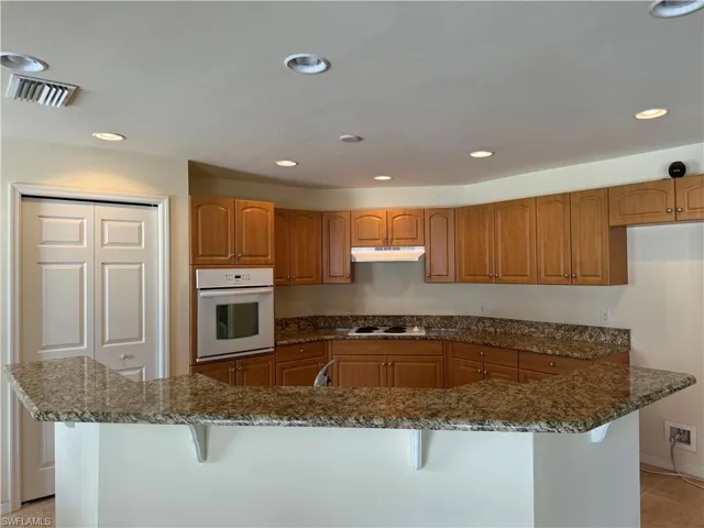 Kitchen with granite countertops, a breakfast bar, white appliances, and light tile patterned floors