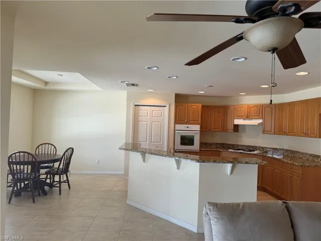 Kitchen with a breakfast bar area, white appliances, light tile patterned floors, dark stone counters, and ceiling fan