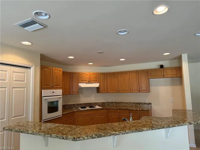Kitchen with a kitchen bar, dark stone counters, white appliances, sink, and kitchen peninsula