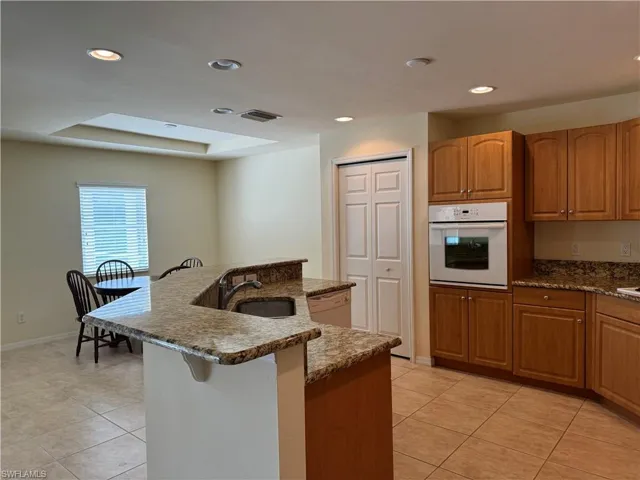 Kitchen featuring white appliances, light tile patterned floors, dark stone counters, a tray ceiling, and sink