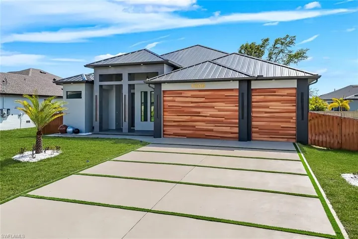 Contemporary house with a garage, a front yard, concrete driveway, a standing seam roof, and a patio