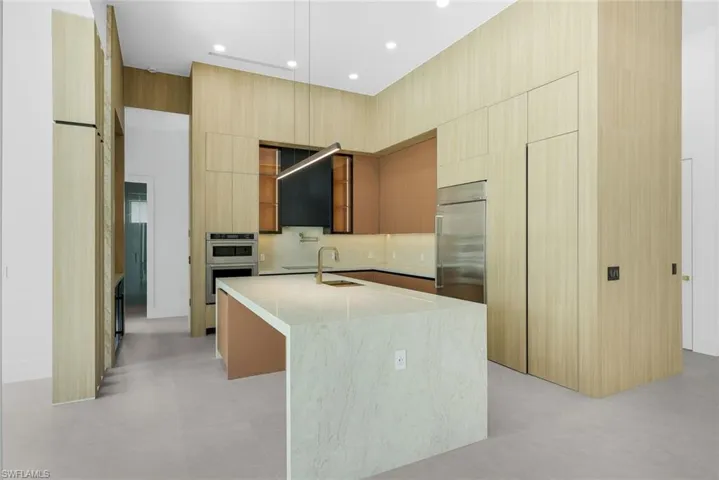 Kitchen with stainless steel appliances, a center island with sink, light stone countertops, light wood finish cabinetry, and modern cabinets