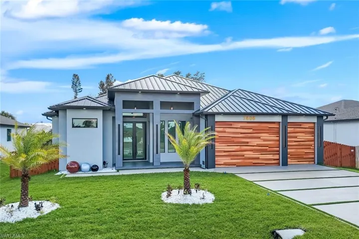 Rear view of property featuring a standing seam roof, a garage, driveway, and stucco siding