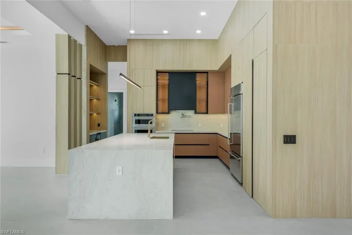 Kitchen with light stone countertops, modern cabinets, open shelves, a kitchen island with sink, and tasteful backsplash