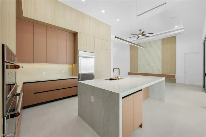 Kitchen with light wood finish cabinets, modern cabinets, light stone counters, a kitchen island with sink, and recessed lighting
