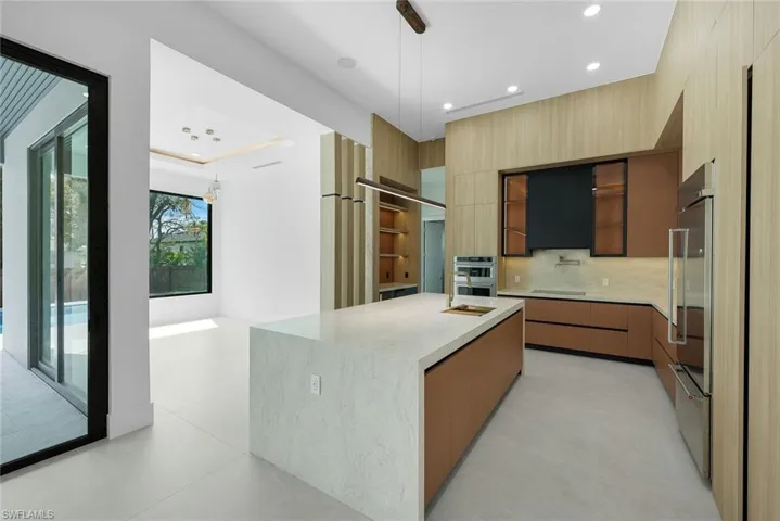 Kitchen featuring modern cabinets, decorative light fixtures, light stone counters, an island with sink, and stainless steel appliances