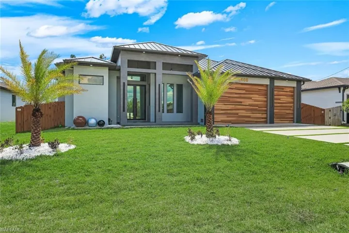 Rear view of house with a standing seam roof, stucco siding, an attached garage, driveway, and a patio