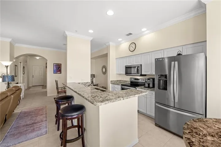 Kitchen with appliances with stainless steel finishes, light stone countertops, crown molding, arched walkways, and light tile patterned floors