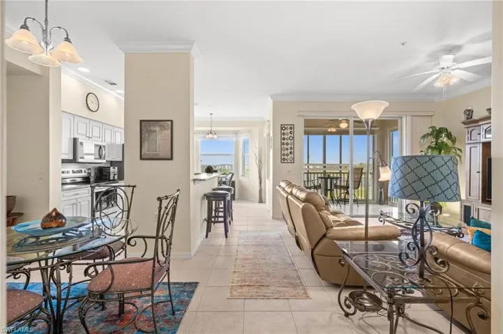 Living area with light tile patterned flooring, a chandelier, crown molding, and a ceiling fan