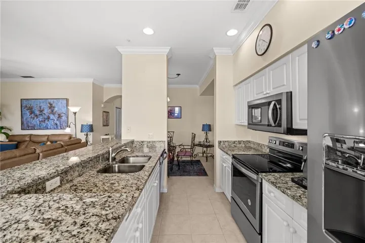 Kitchen with appliances with stainless steel finishes, arched walkways, light stone counters, white cabinets, and ornamental molding