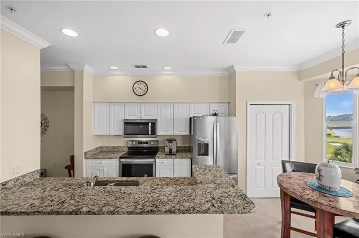 Kitchen with a peninsula, dark stone counters, stainless steel appliances, ornamental molding, and pendant lighting