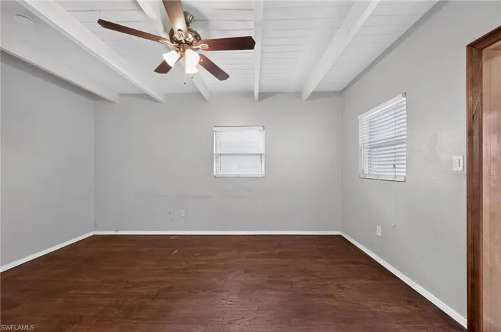 Spacious room featuring wood-finish flooring, light grey walls, and a white plank and beam ceiling