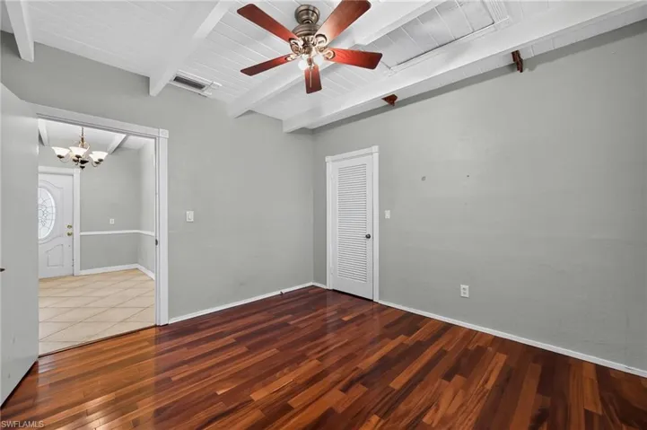 Spacious room featuring wood-finish flooring, vaulted ceiling with exposed beams, and a ceiling fan with integrated lighting