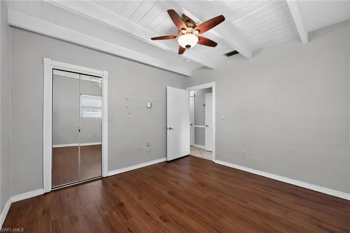 Room featuring wood-finish flooring, a white vaulted ceiling with exposed beams, and a ceiling fan with integrated lighting