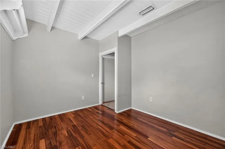 Vaulted ceiling featuring exposed beams, wood-finish flooring, light gray wall paint, and white trim