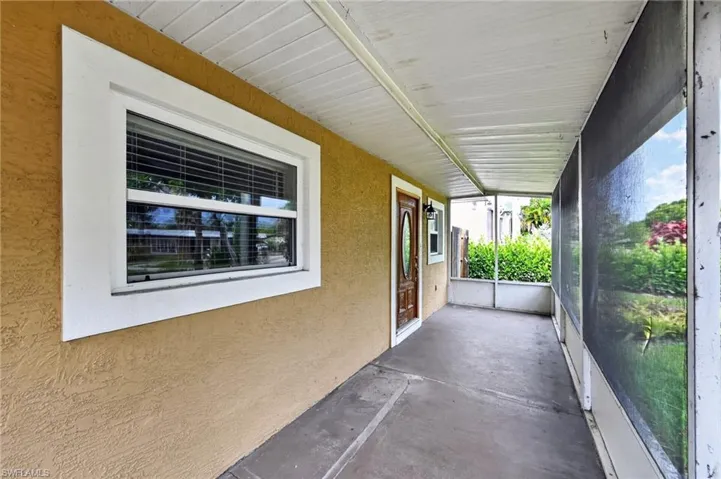 Screened porch featuring a wood-panel entry door, textured stucco exterior, and white vinyl windows