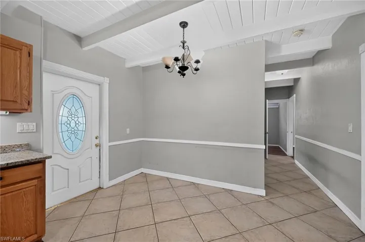 Spacious room featuring tile flooring, exposed ceiling beams, a decorative chandelier, and a white door with a stained-glass oval insert