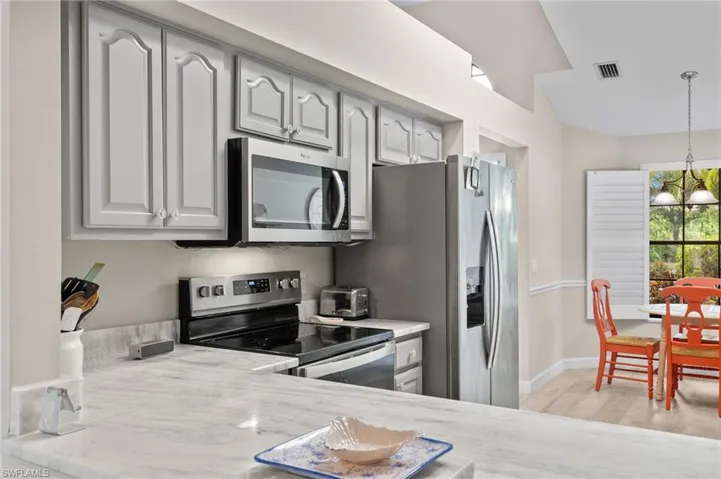 Kitchen featuring stainless steel appliances, decorative light fixtures, light wood-type flooring, and light stone countertops
