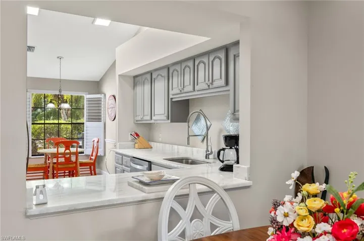 Kitchen featuring dishwasher, a chandelier, sink, light stone countertops, and gray cabinetry