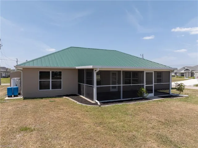 Back of property with stucco siding, a lawn, a sunroom, and metal roof