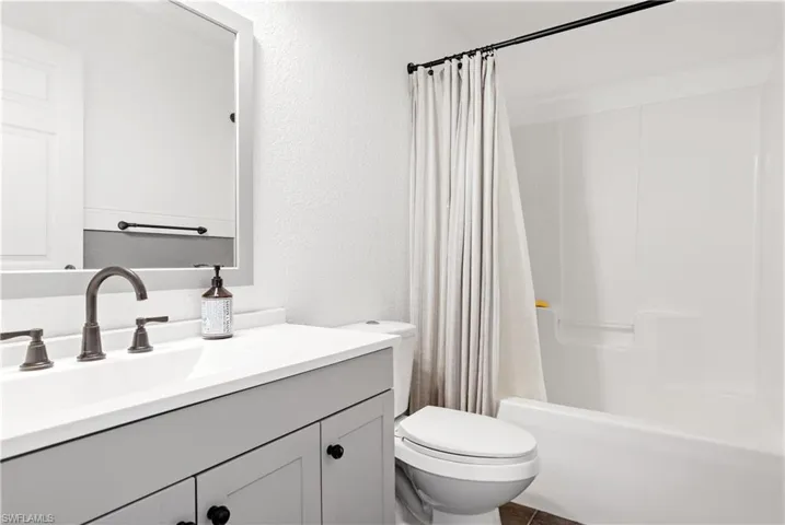 Full bath with shower / bath combination with curtain, a textured wall, vanity, and toilet