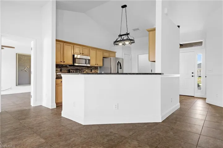Kitchen featuring backsplash, dark countertops, visible vents, hanging light fixtures, and appliances with stainless steel finishes