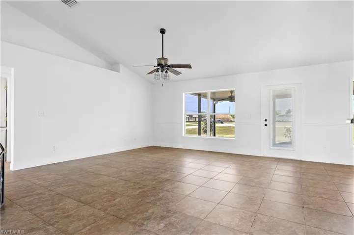 Tiled empty room with vaulted ceiling, visible vents, a ceiling fan, and baseboards