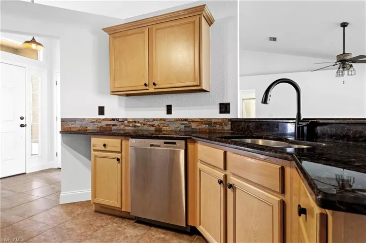 Kitchen featuring stainless steel dishwasher, a sink, dark stone counters, and a ceiling fan