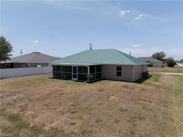 Back of property featuring central air condition unit, metal roof, fence, a lawn, and a sunroom