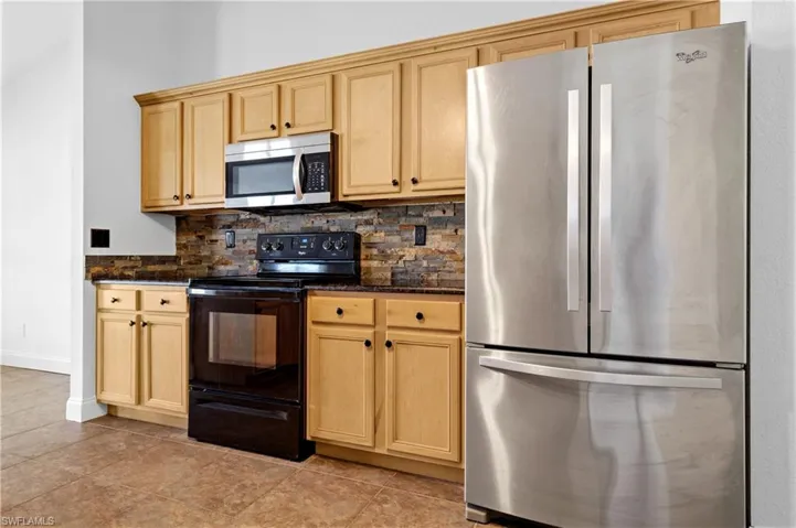Kitchen featuring stainless steel appliances, dark stone counters, baseboards, decorative backsplash, and light brown cabinets