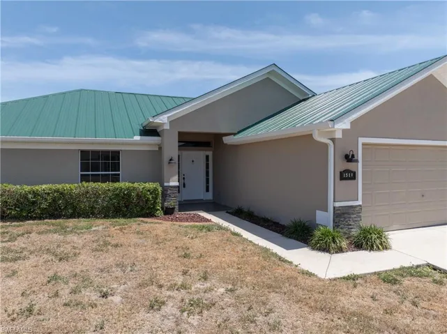Ranch-style home with stone siding, metal roof, a garage, and stucco siding
