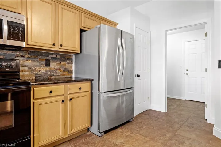 Kitchen featuring dark stone counters, decorative backsplash, light brown cabinetry, stainless steel appliances, and baseboards