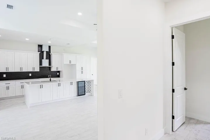 Kitchen with tasteful backsplash, wall chimney range hood, sink, wine cooler, and a kitchen island with sink