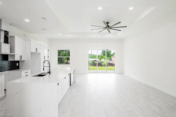 Kitchen with ceiling fan, a tray ceiling, decorative backsplash, sink, and light hardwood / wood-style flooring