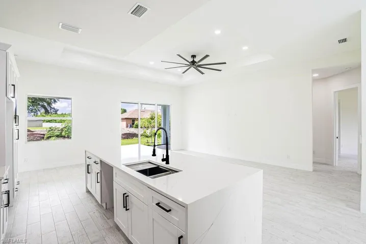 Kitchen featuring sink, ceiling fan, a raised ceiling, and an island with sink