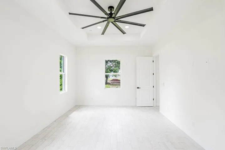 Unfurnished room with light wood-type flooring, ceiling fan, and a raised ceiling