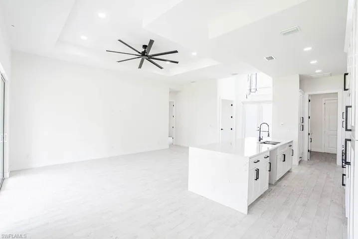 Kitchen with light hardwood / wood-style flooring, sink, ceiling fan, white cabinetry, and a tray ceiling
