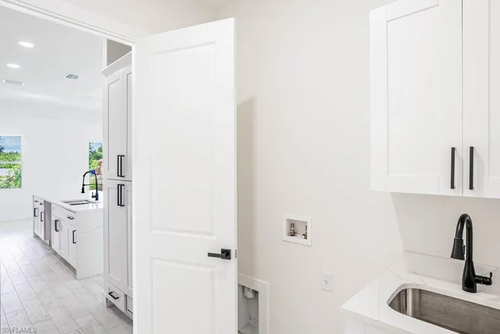 Laundry area with washer hookup, sink, cabinets, and light hardwood / wood-style floors