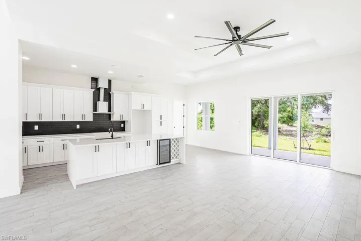 Kitchen with white cabinetry, beverage cooler, a tray ceiling, sink, and a center island with sink