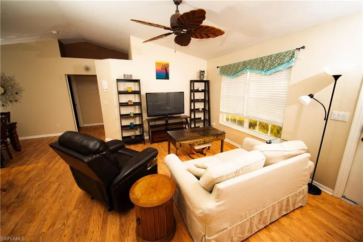 Living room with hardwood / wood-style floors, vaulted ceiling, and ceiling fan