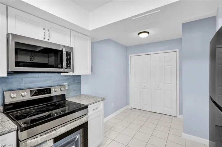 Kitchen with stainless steel appliances, white cabinets, light tile patterned floors, light stone countertops, and tasteful backsplash